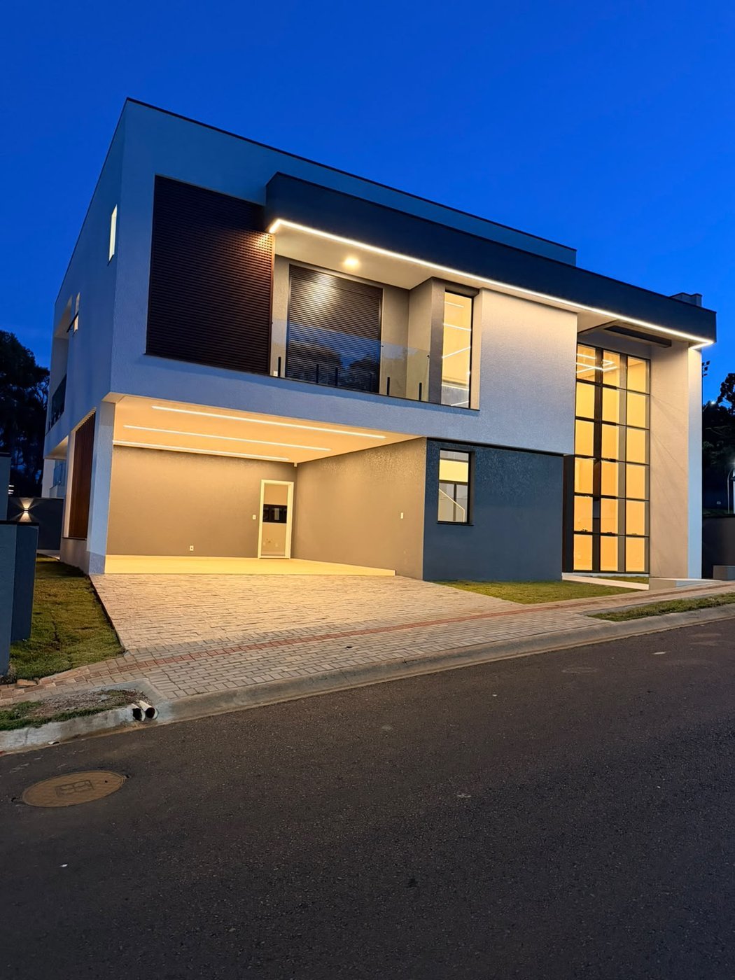 Fachada em perspectiva ao anoitecer, com garagem ampla e amplos vãos de vidro iluminados